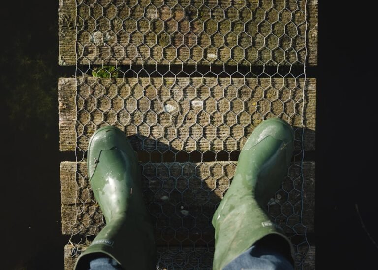 Overhead view of green rubber boots on a weathered wooden bridge.