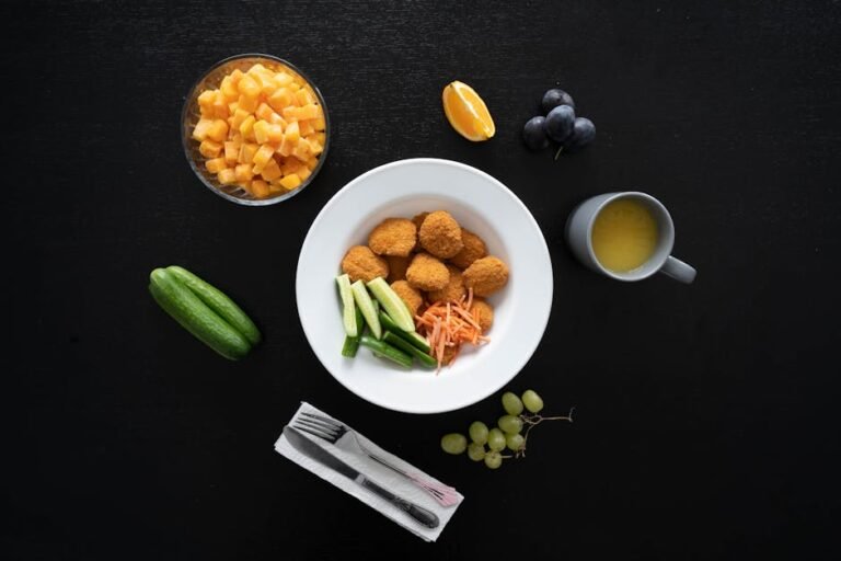 Healthy meal with chicken nuggets, fruits, and vegetables arranged on a black background.