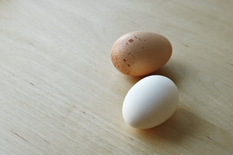 Close-up view of a brown and a white chicken egg resting on a wooden surface. Perfect for culinary concepts.