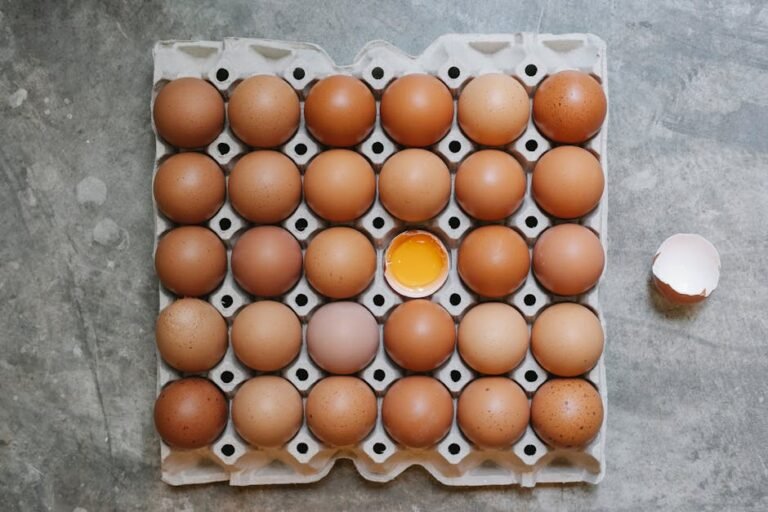 Top view of chicken eggs placed in cardboard container with cracked eggshell on table