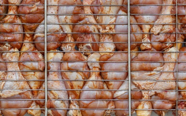 Top view background of raw chicken drumsticks with skin and condiments under metal rack in daytime